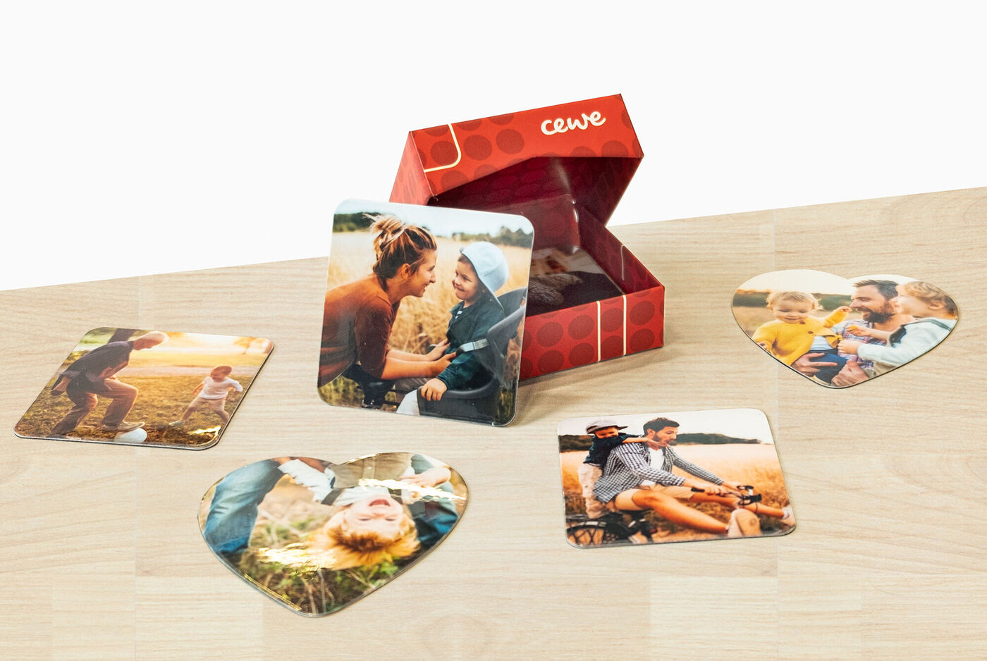 Tarjetas fotográficas en forma de corazón junto a una caja de regalo de CEWE, llena de recuerdos.