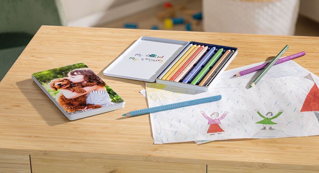 Un álbum CEWE sobre una mesa de madera junto a lápices y dibujos de niños.