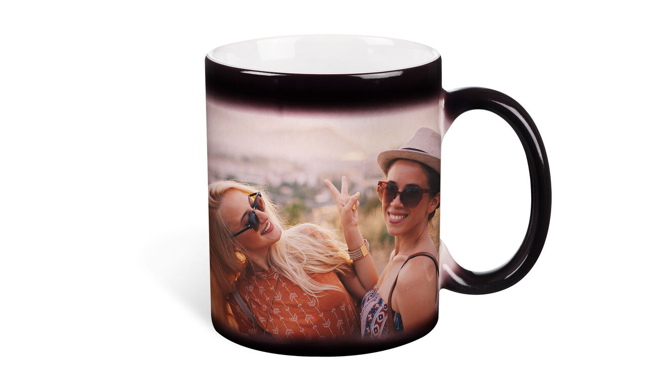 Dos mujeres sonríen y posan felices con gafas de sol en un lugar pintoresco, una sostiene una taza