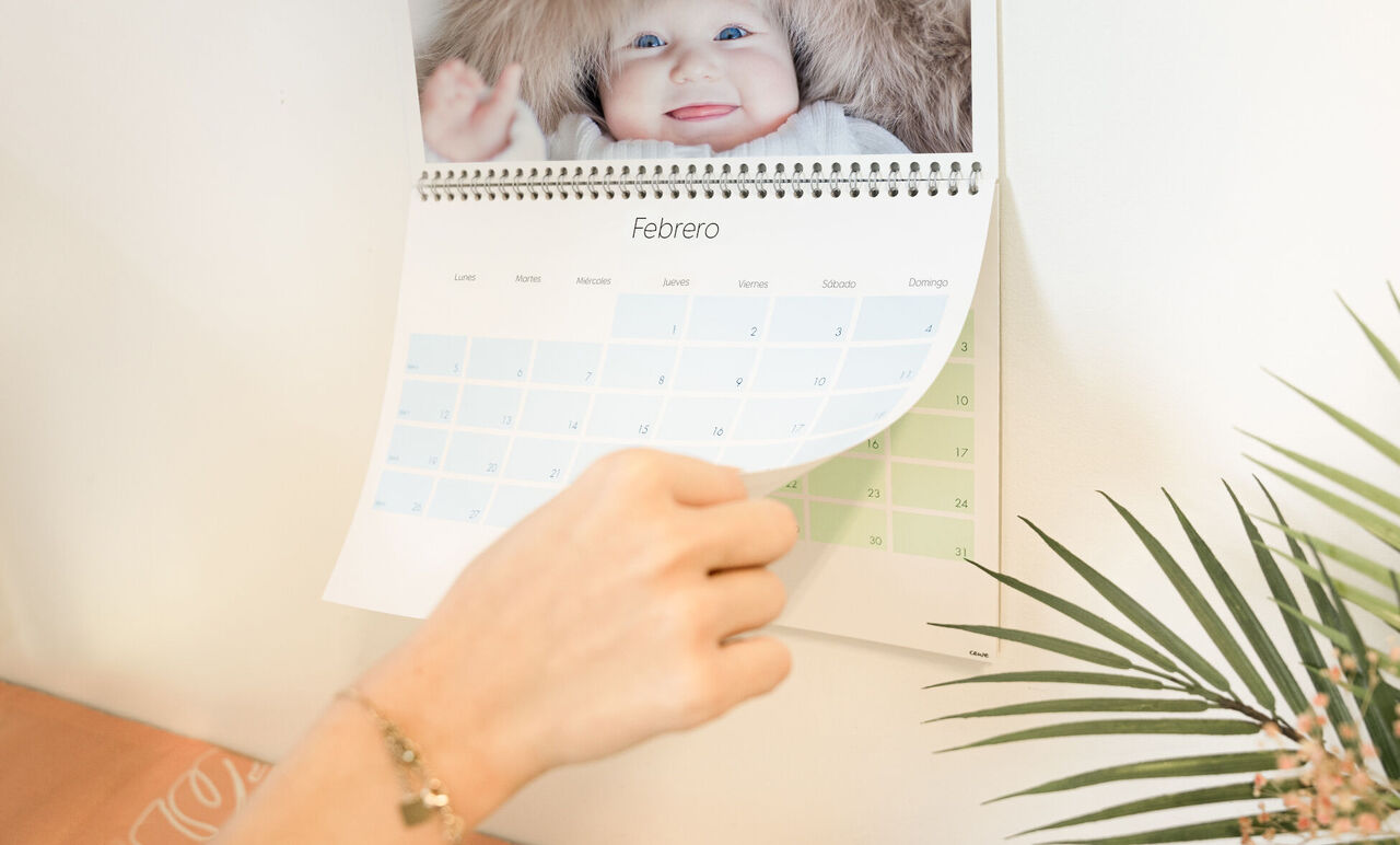 Una mano hojea un calendario CEWE, visible el mes de febrero.