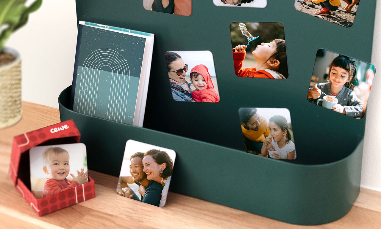 Una pared con fotos coloridas, incluyendo un álbum CEWE y una pequeña caja de regalo.