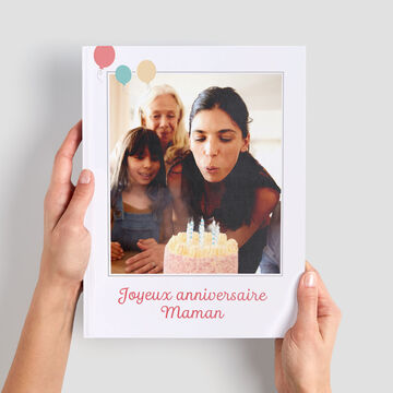 Una persona sostiene un fotolibro de una fiesta de cumpleaños. Hay velas en el pastel.