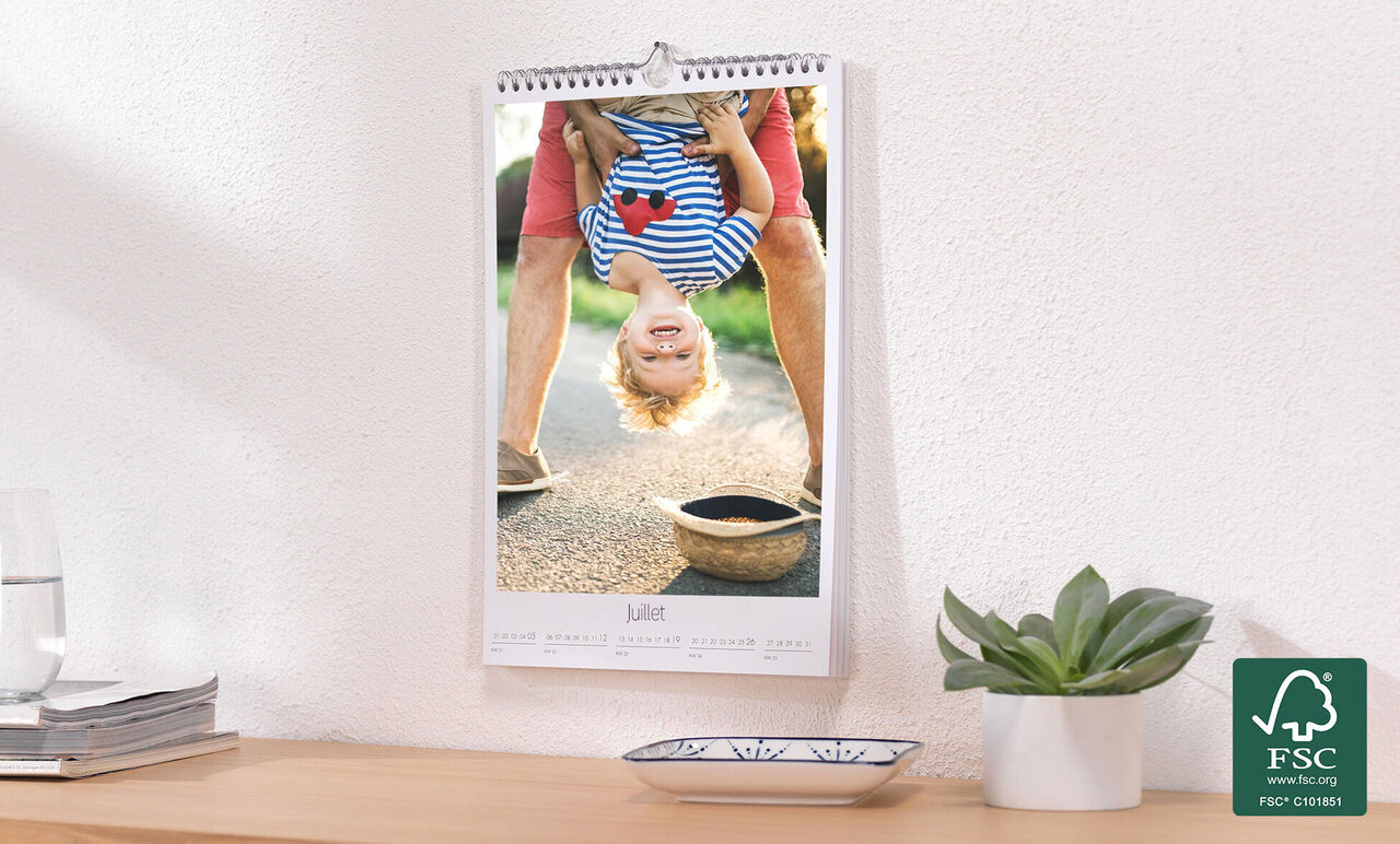 Un niño feliz cuelga cabeza abajo de un calendario. Lleva una camiseta a rayas y sonríe.
