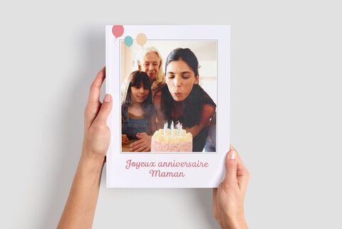 Una persona sostiene un CEWE Fotolibro de una fiesta de cumpleaños. Hay un pastel y velas visibles. Es un momento cálido.
