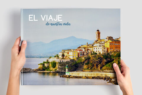 Alguien sostiene un álbum CEWE con un colorido paisaje costero.