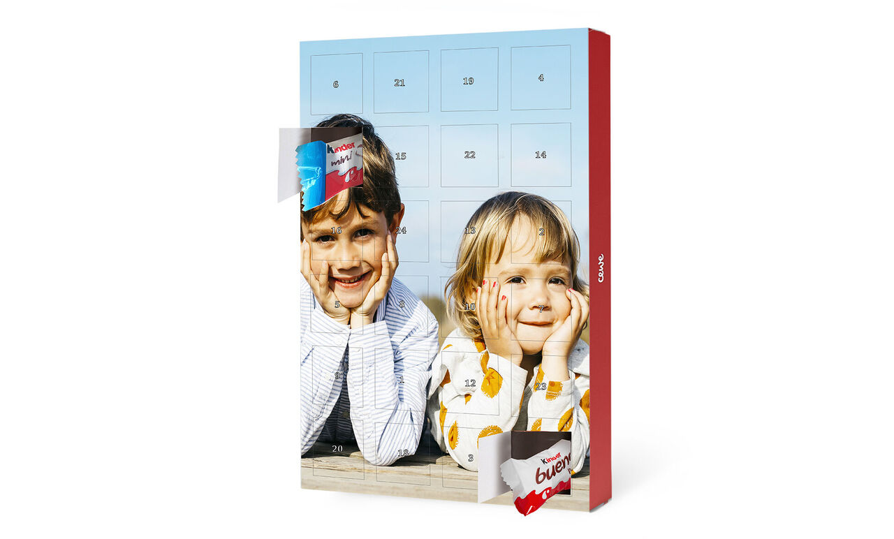 Dos personas sonríen detrás de un calendario de adviento iluminado por el sol.