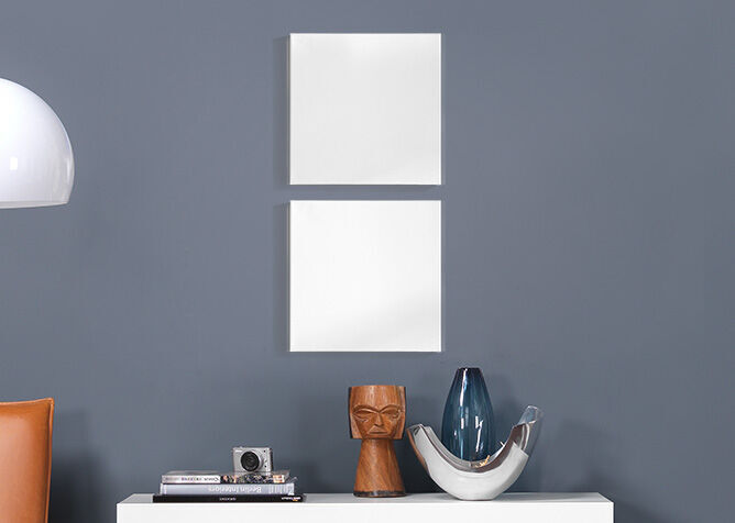 Dos marcos blancos vacíos en una pared gris sobre una mesa con objetos decorativos.