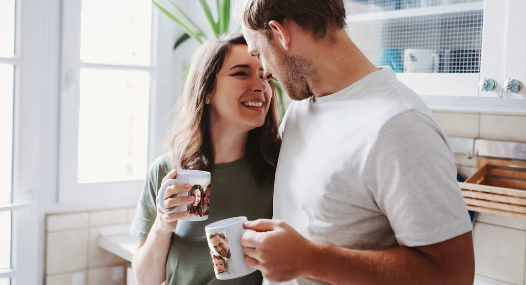 Una pareja disfruta de un momento juntos en la cocina con tazas fotográficas en las manos.