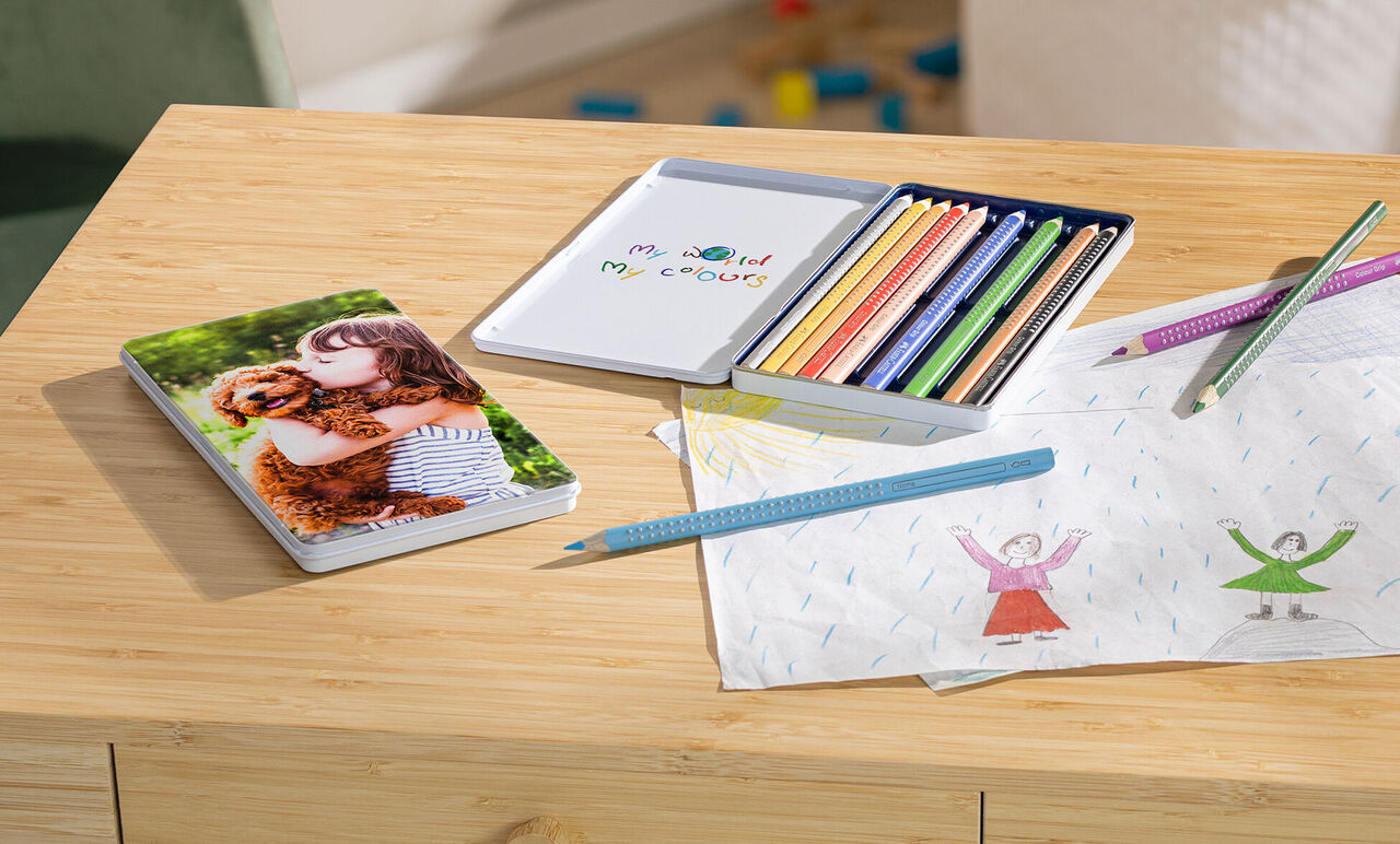 Un niño abraza a un perro sobre un álbum. Lápices de colores y un bloc de dibujo en la mesa.