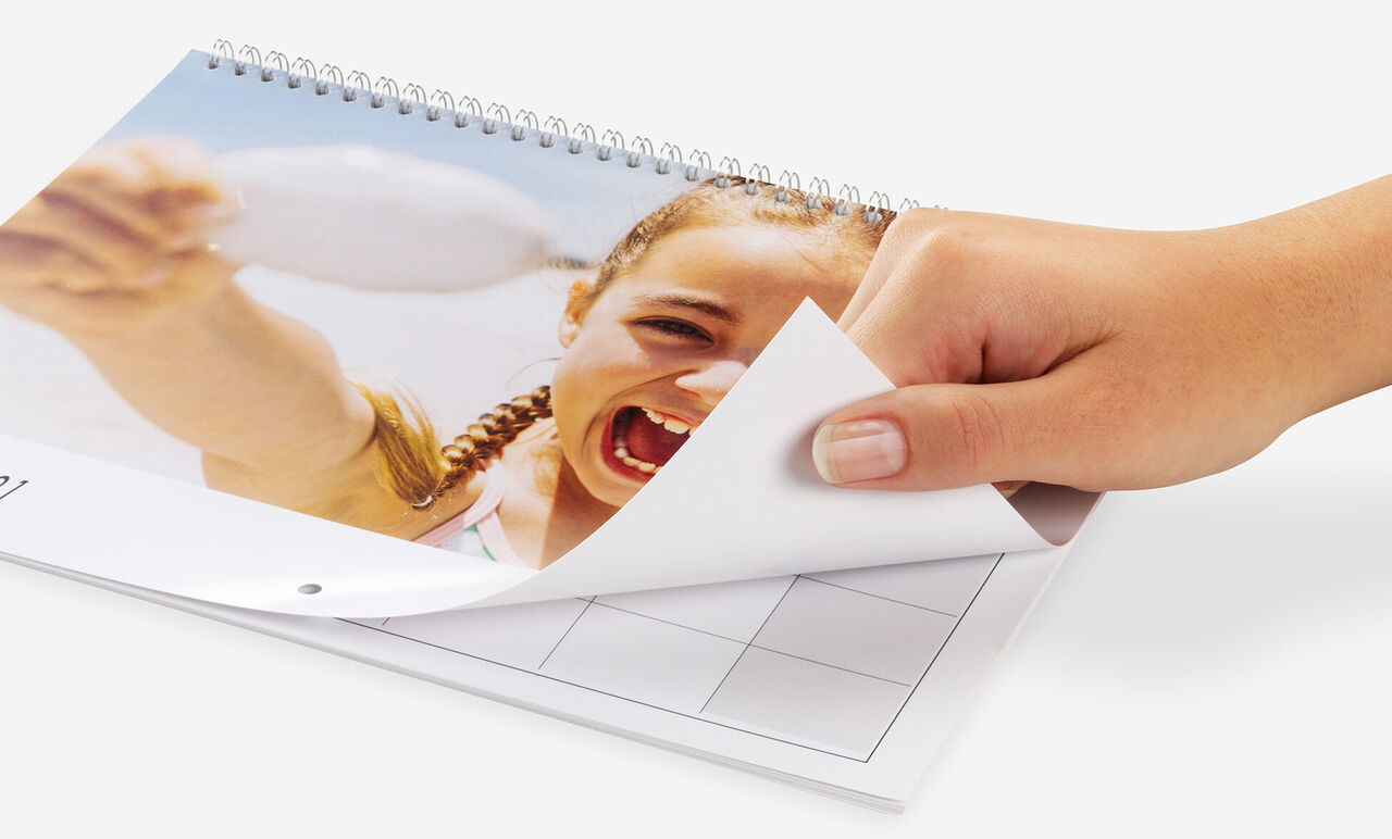 Una mano pasa páginas de un calendario fotográfico CEWE con un bonito motivo.