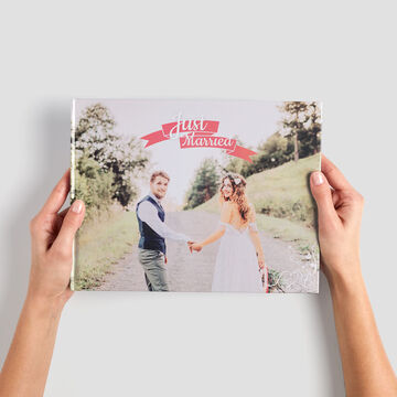 Una novia y un novio se toman de la mano y sonríen en la portada de un libro de fotos CEWE titulado 'Recién Casados'