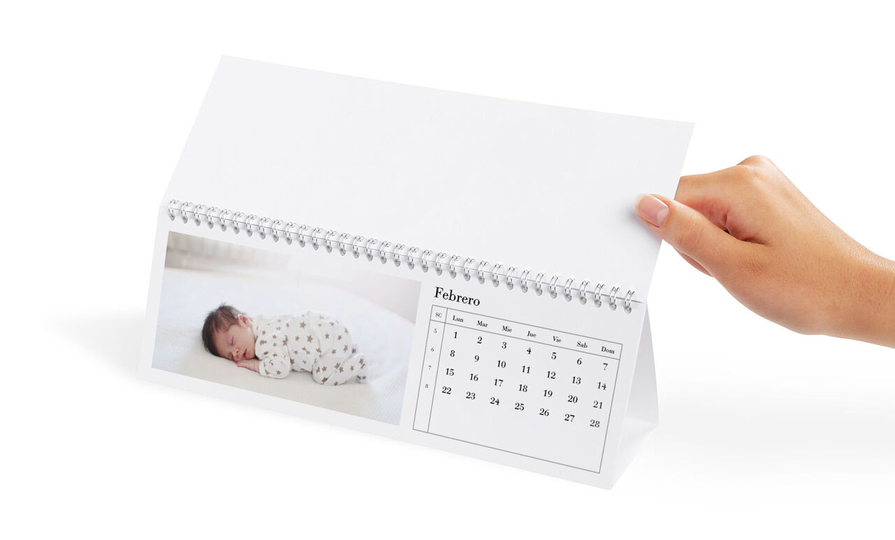 Calendario con una foto de bebé, colores suaves, mano lo sostiene.