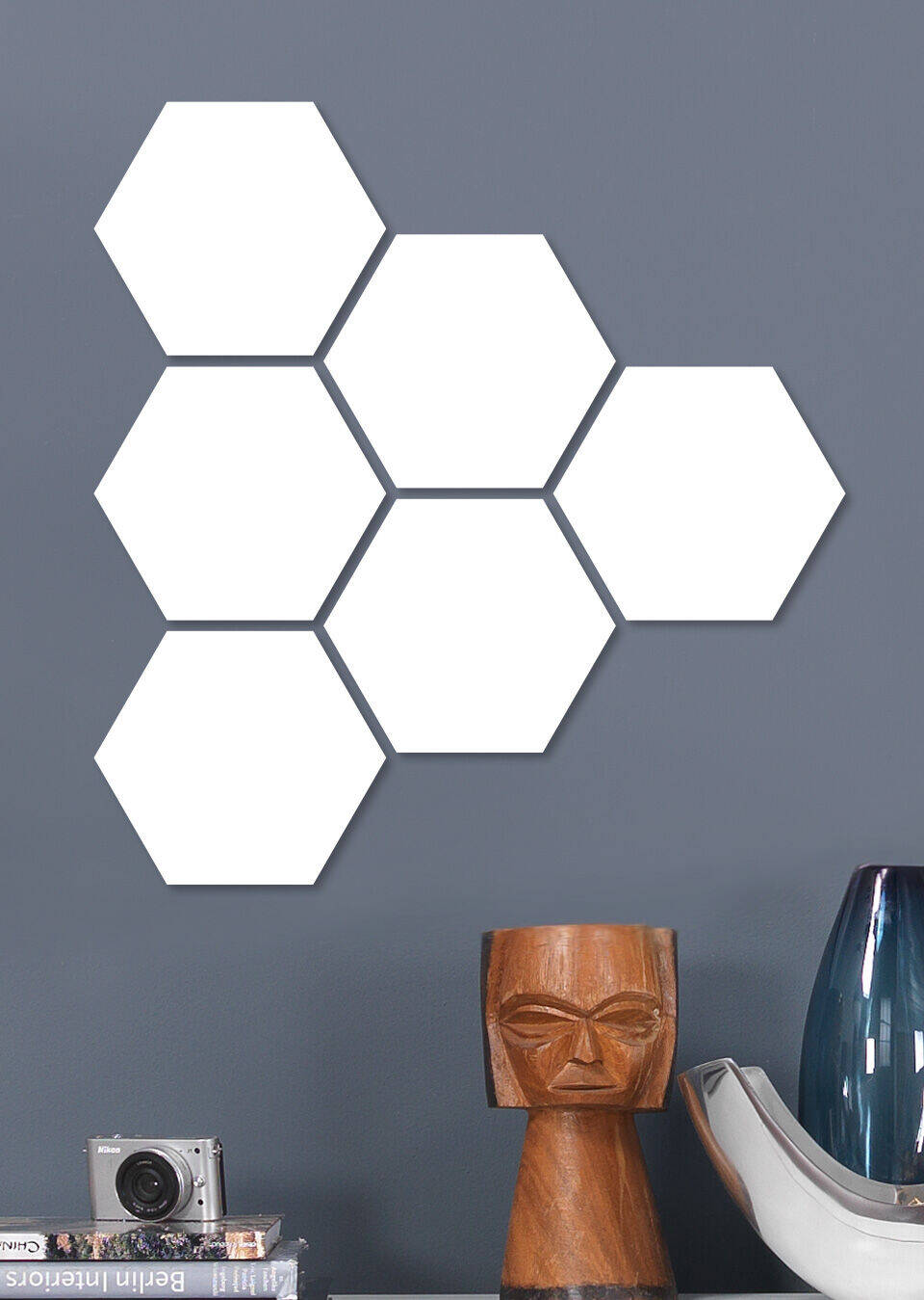 Seis formas hexagonales blancas en una pared gris, al lado una lámpara moderna y una cámara