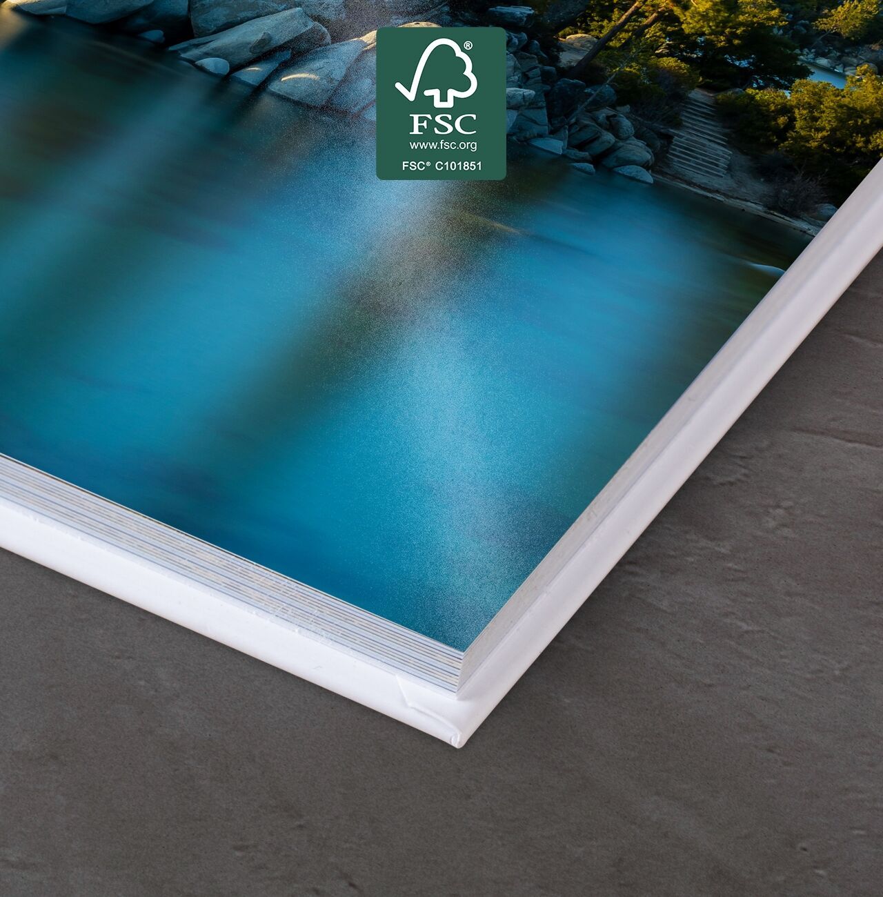 Primer plano de un fotolibro CEWE sobre una mesa con agua azul de fondo