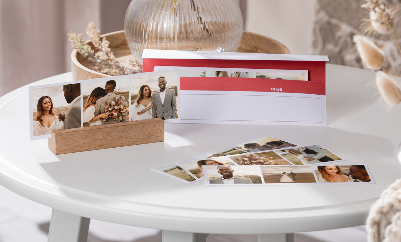 Un calendario fotográfico CEWE elegantemente presentado sobre una mesa con fotos de una boda.