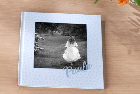 Un álbum CEWE con una niña en un vestido blanco corriendo al aire libre. En la portada está el nombre 'Paula'.