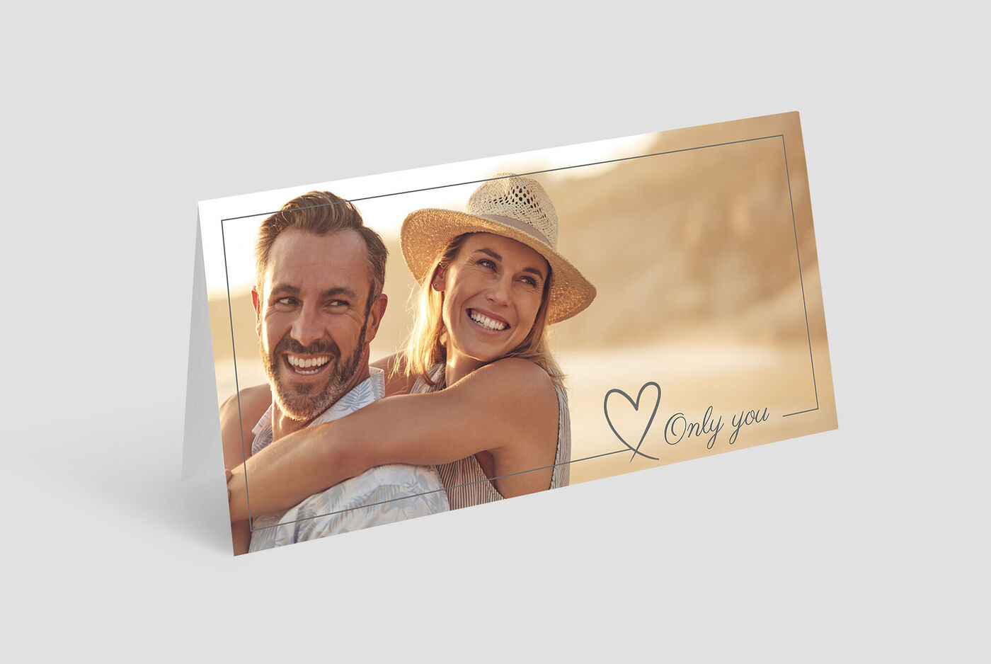 Dos personas abrazándose al aire libre, con sombrero de sol, fondo de playa.