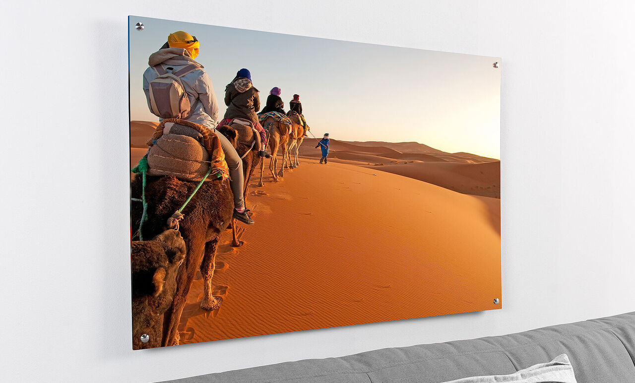 Un grupo de personas monta camellos a través de un soleado paisaje desértico. Las dunas brillan en naranja.