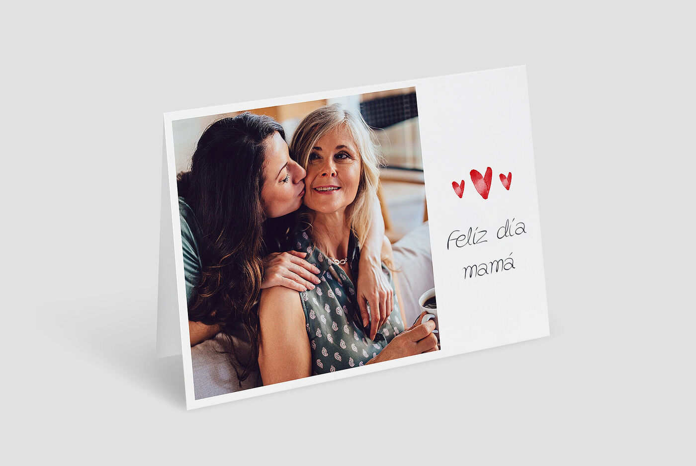 Dos mujeres se abrazan, una sostiene un café. En el fondo hay un ambiente cálido con decoración.
