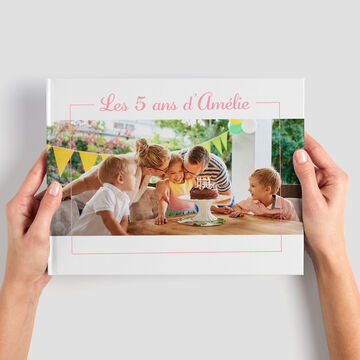 Una persona muestra un álbum CEWE con una colorida portada sobre un cumpleaños con niños.