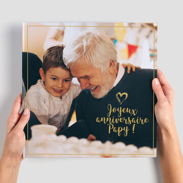Dos personas sostienen un álbum con una portada tierna. Inscripción: '¡Feliz cumpleaños Papi!'