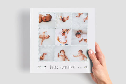 Una persona sostiene un álbum CEWE con maravillosas fotos de bebés en suaves colores. Cada página muestra diferentes momentos.