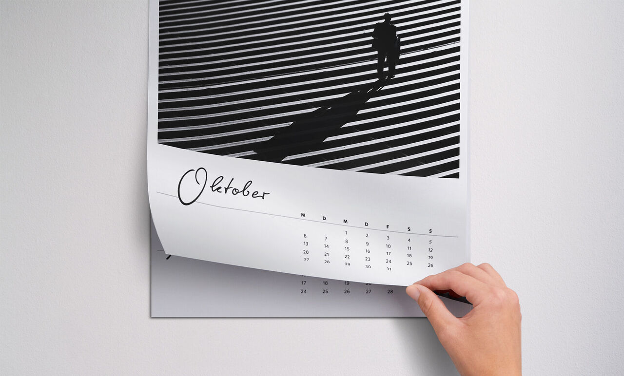 Una mano pasa la página de un calendario con líneas en blanco y negro y una persona en sombra. El mes de octubre es visible.