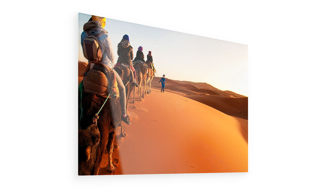 Seis personas montan camellos sobre las dunas del desierto al atardecer.