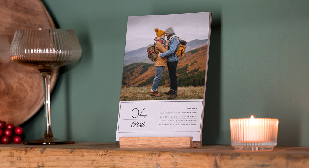 Una pareja se abraza sobre un calendario, con vela y vaso al fondo.