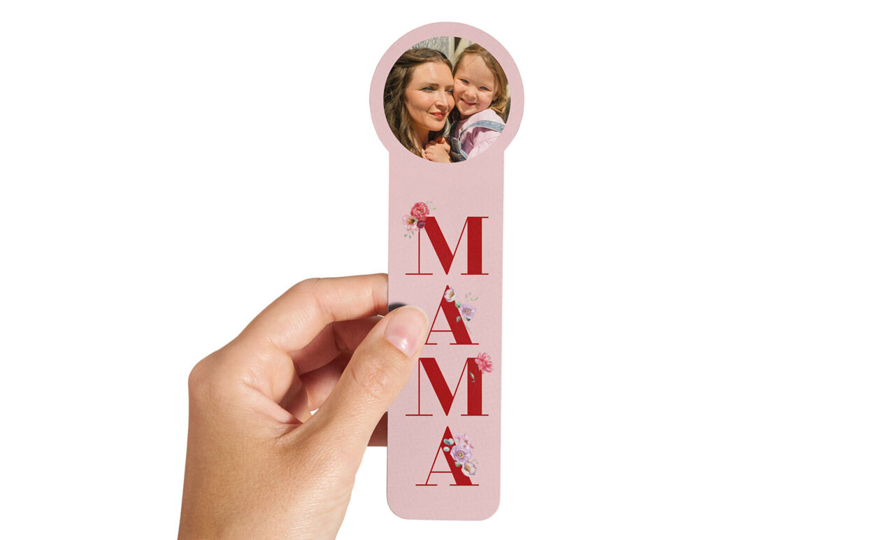 Marcapáginas rosa personalizado con texto 'MAMÁ' y foto circular de una madre con su hija, sostenido en una mano