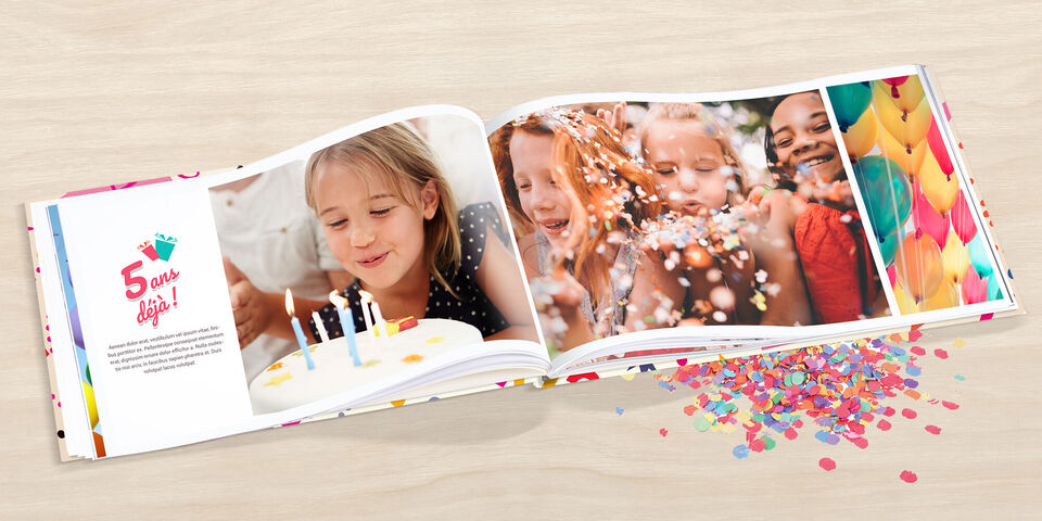 Un fotolibro abierto con imágenes coloridas de una fiesta. El pastel y las velas son visibles, rodeados de confeti.