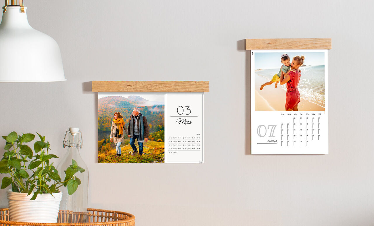 Dos calendarios CEWE cuelgan en una pared. El calendario de la izquierda muestra una pareja al aire libre, el de la derecha una familia en la playa.