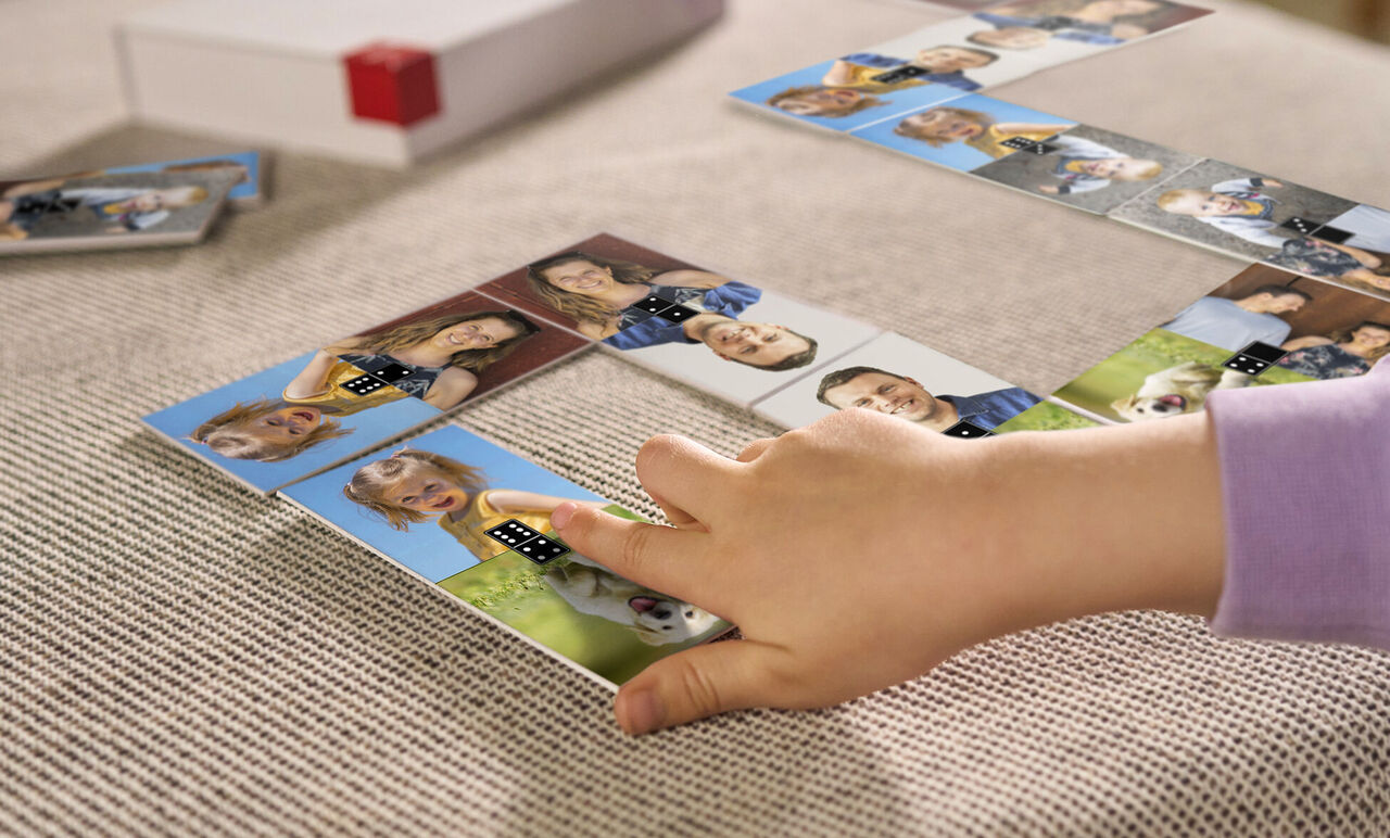 Un niño juega con fichas de dominó personalizadas en una mesa, mostrando fotos de amigos y familia.