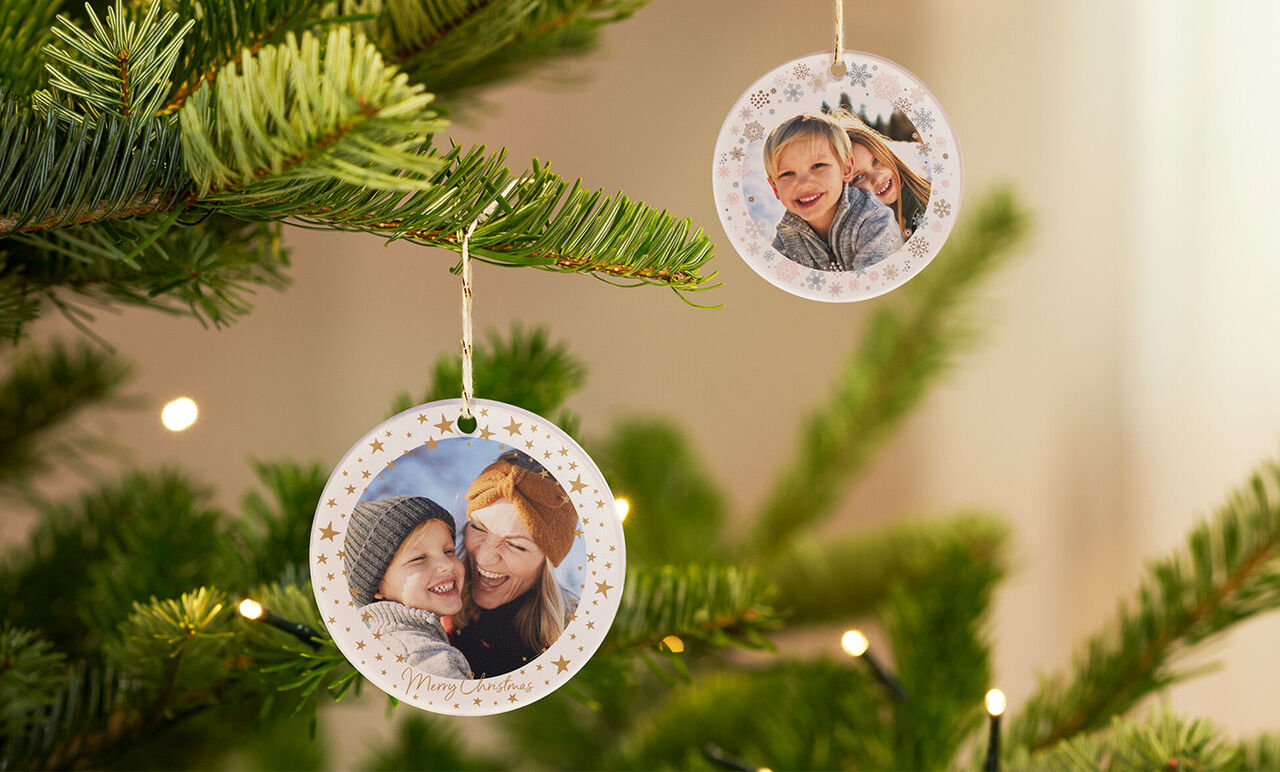 Dos adornos de árbol de Navidad redondos con fotos personales cuelgan de un abeto.