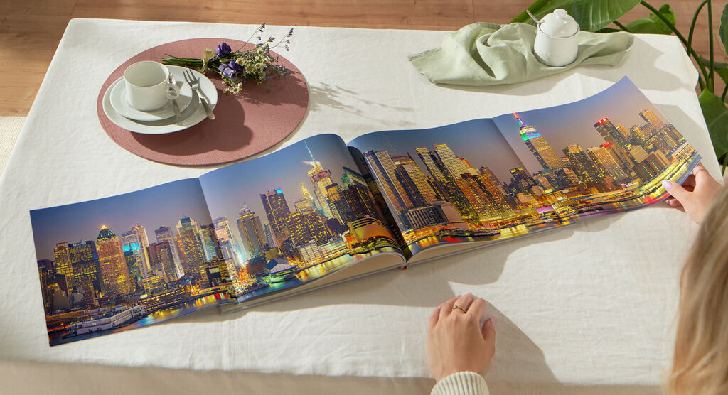 Una persona pasa las páginas de un fotolibro abierto con una vista nocturna de Filadelfia sobre una mesa.